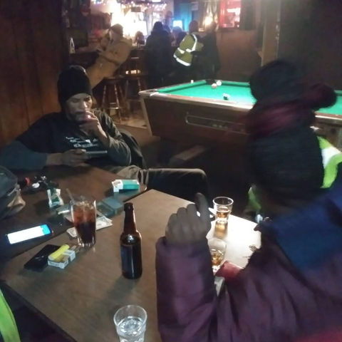 People drinking and smoking at a table inside The Ugly Broad.