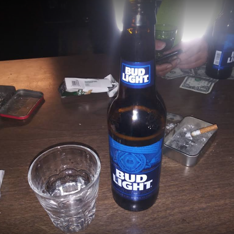 Close-up of a glass, a Bud Light bottle, and an ashtray on a table.
